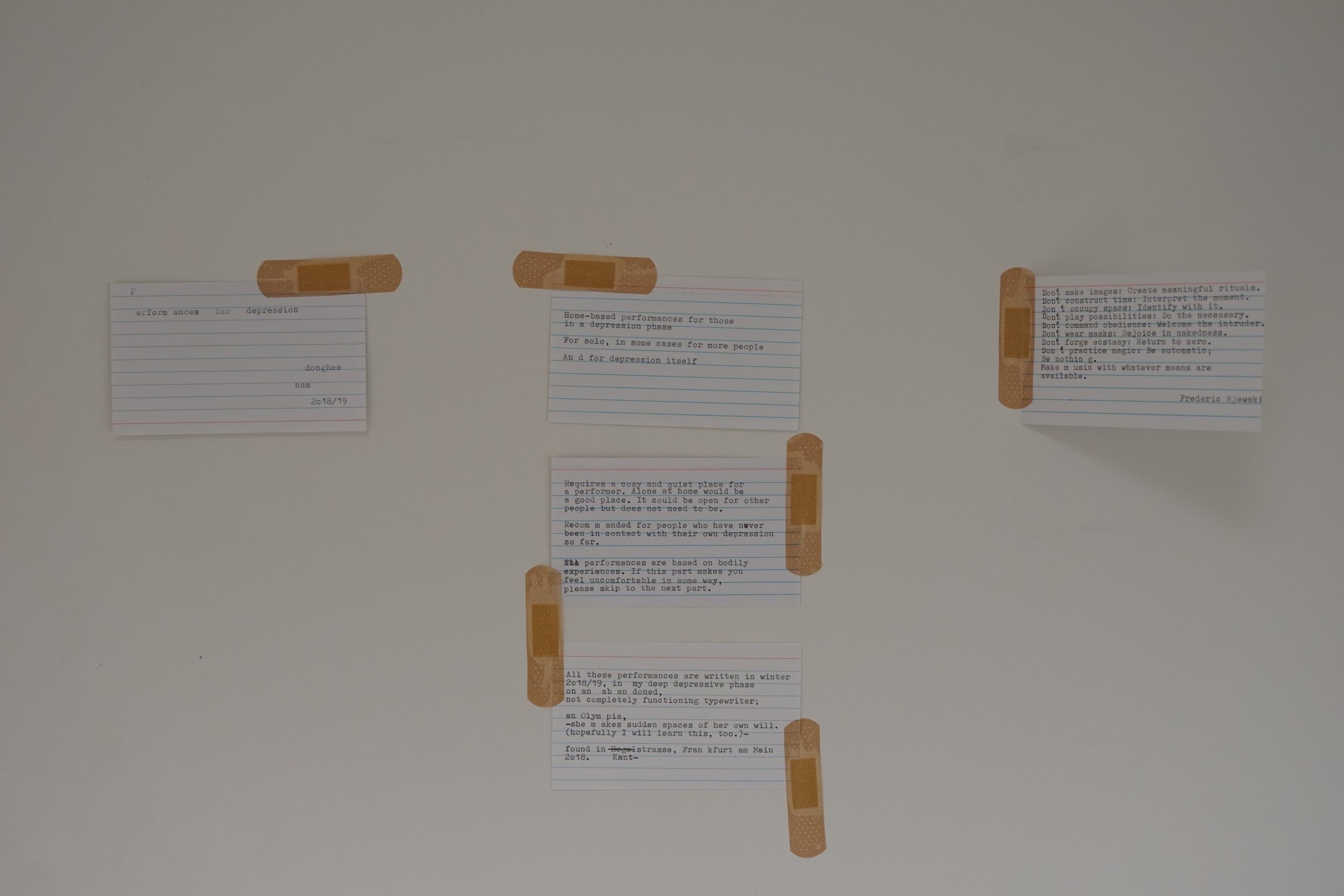 Index cards with typed text on a white wall, each held in place with plasters