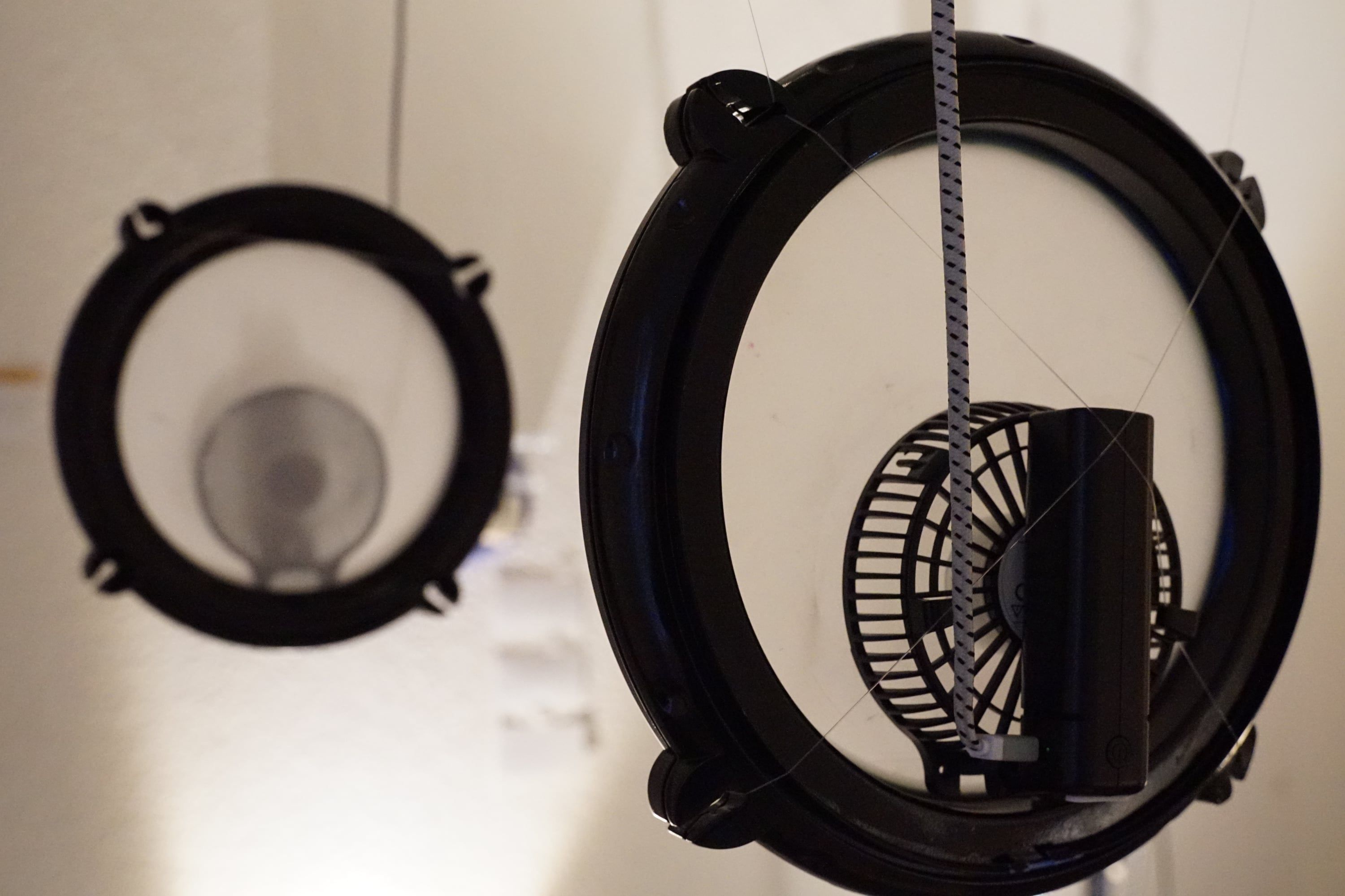 Two black hoops hanging from the ceiling, in the nearer one a small black fan on a cord, the farther one out of focus