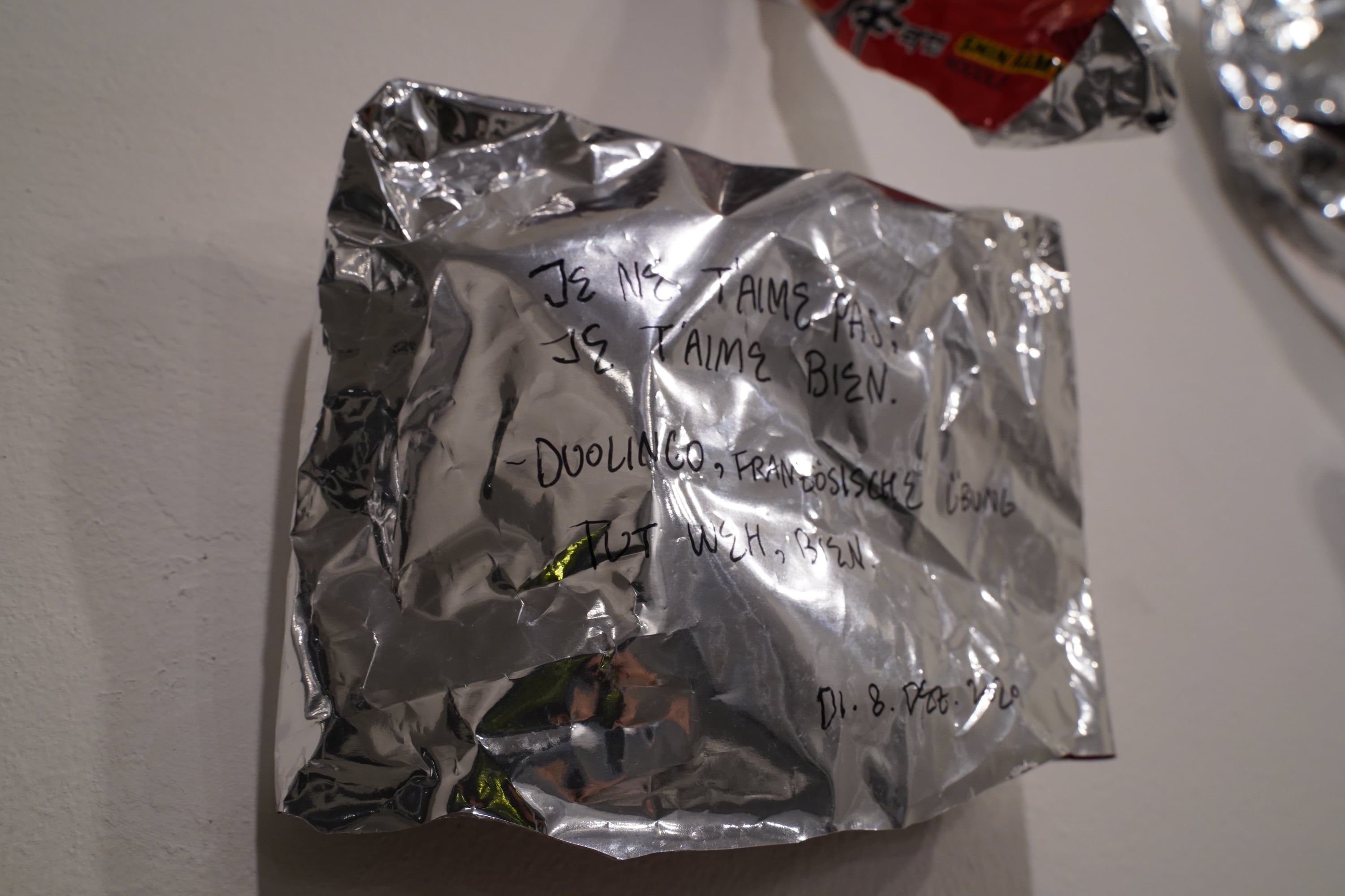 A crumpled piece of aluminium foil on the wall, written on by hand with a black pen.