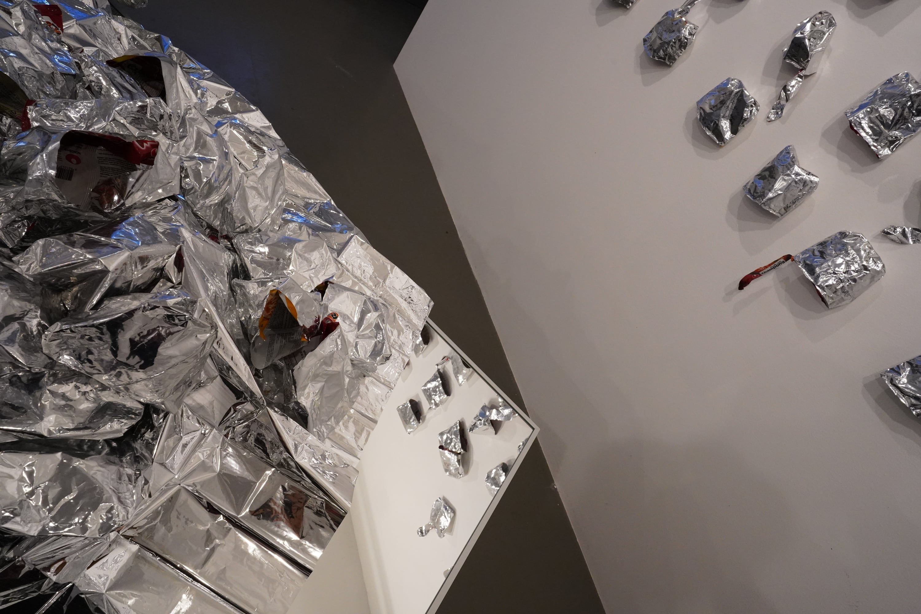 Seen from above, the heap of crumpled aluminium foil on the table, at the right the wall with its aluminium pieces.