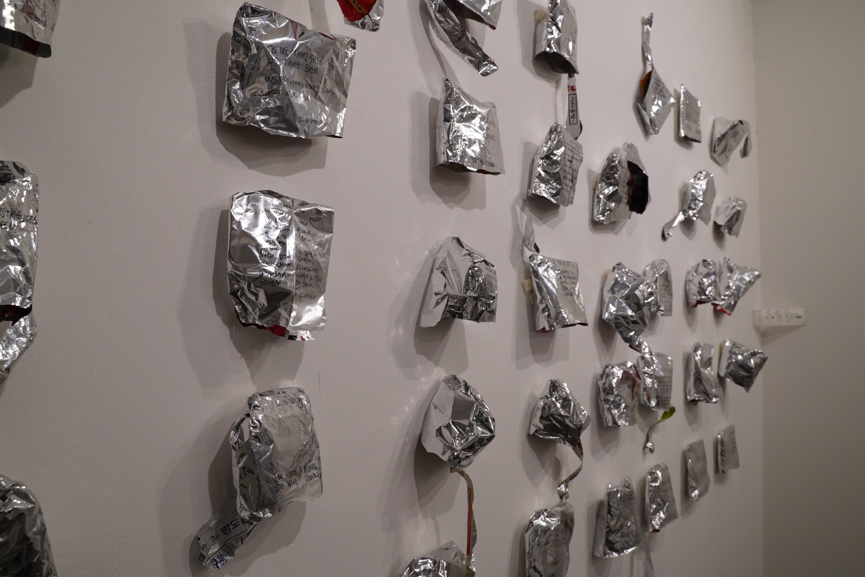 An oblique view of the wall: crumpled aluminium packets in rows on a white wall.
