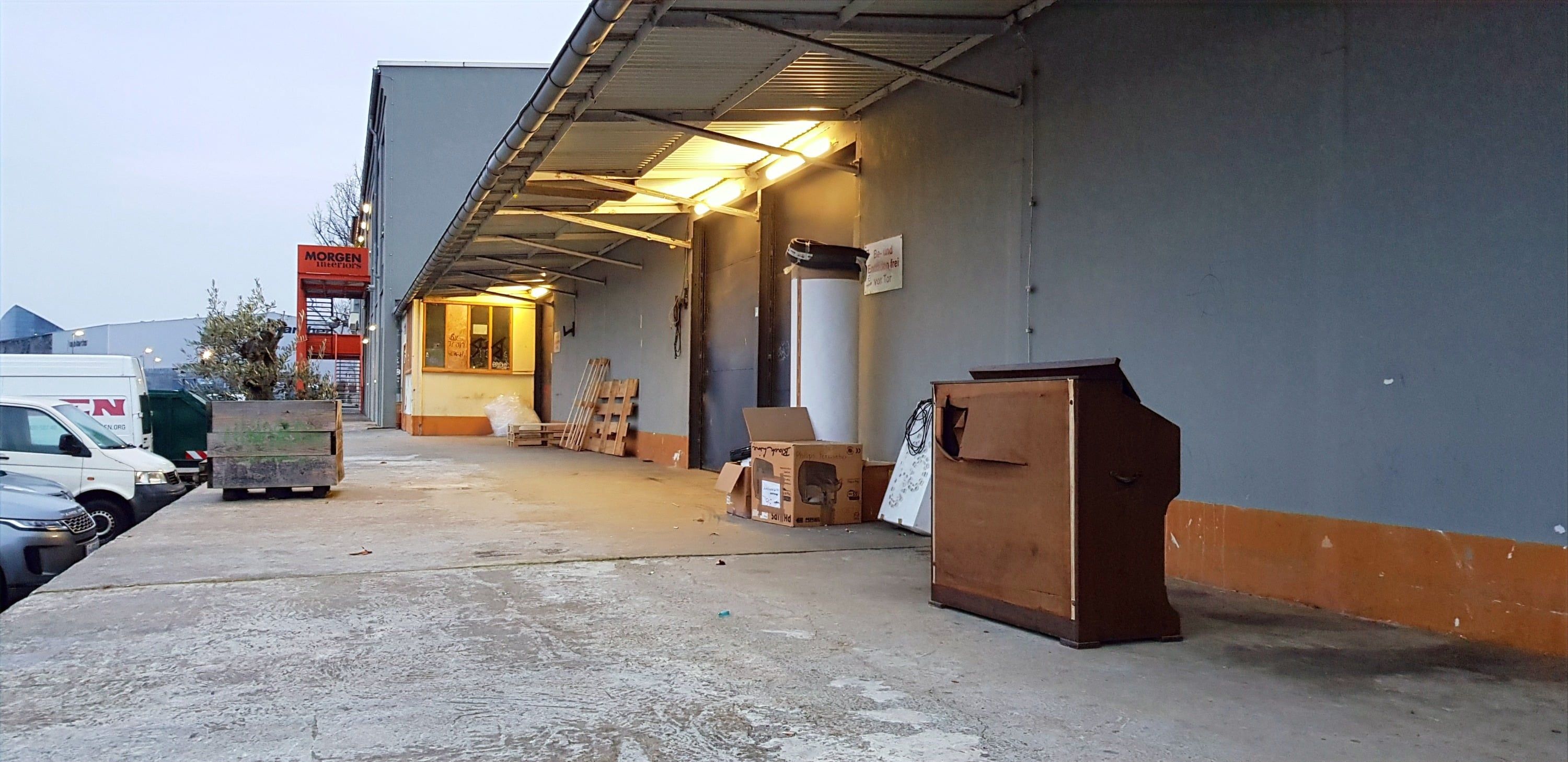 Dasselbe Harmonium im Abendlicht vor der grauen Wand einer Lagerhalle, daneben abgestellte Kartons.