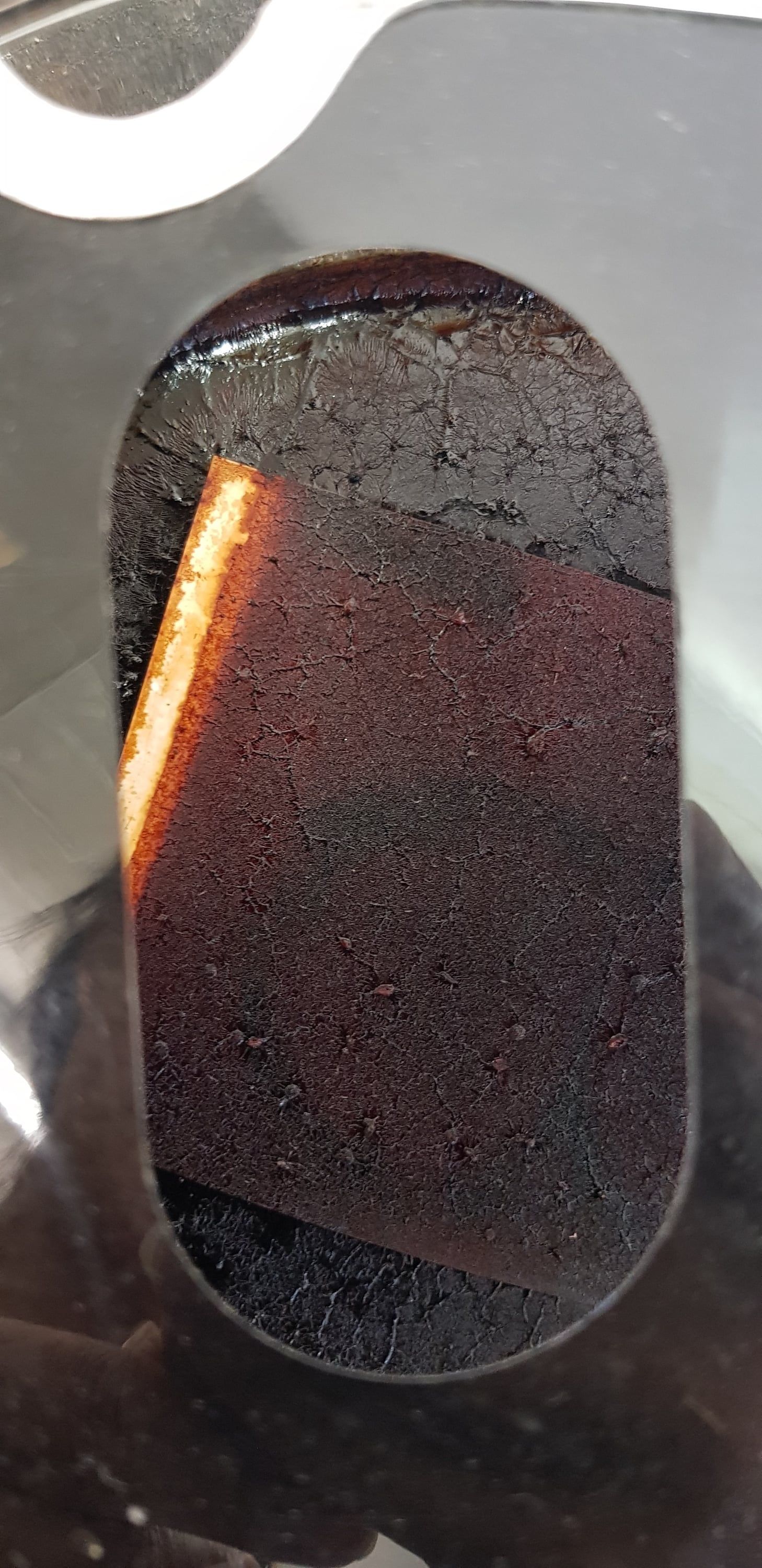 Blick durch eine ovale Öffnung in das linke Objekt: eine dunkle Schale mit einer rostfarbenen Platte, von der Seite hell angestrahlt.