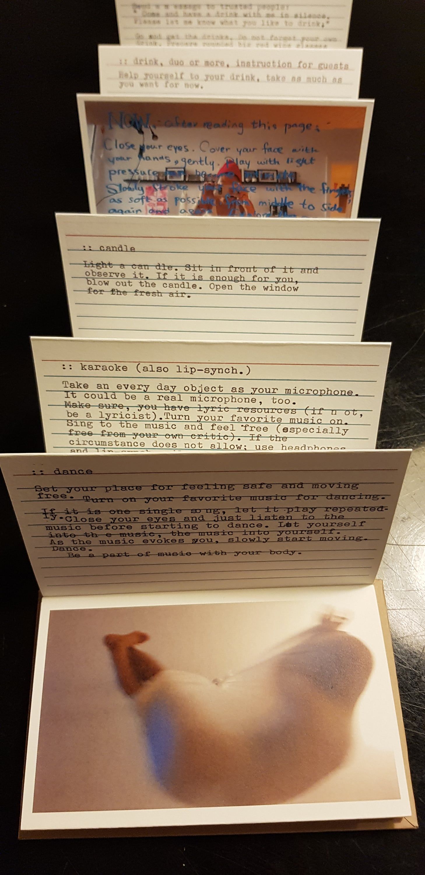The booklet pulled open like an accordion against a black background: typed index cards headed candle, karaoke and dance, and at the front a photograph of a body wrapped in a translucent cloth.