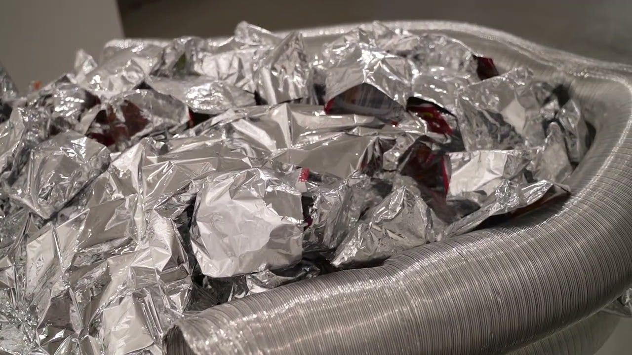 Close view of the heap of crumpled silver foil and bags inside the ring of aluminium duct.